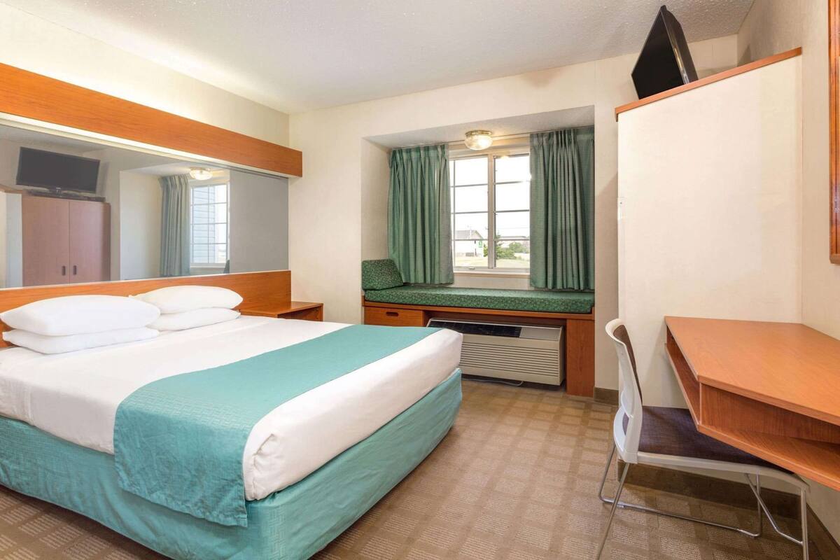 A hotel room with a bed, desk, chair, and a window with curtains.