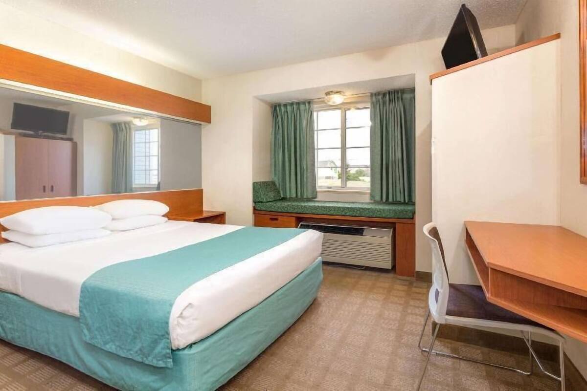 A hotel room with a bed, a desk, a chair, a television, and a window with curtains.
