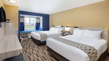 A hotel room with two beds, a desk, a TV, and a window with curtains.