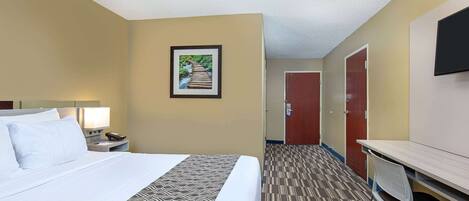 A hotel room with a bed, a desk, a chair, a nightstand, a lamp, and a framed picture on the wall.