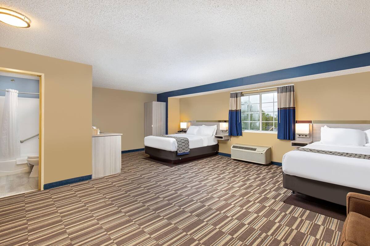 A hotel room with two beds, a bathroom, and a window with curtains.