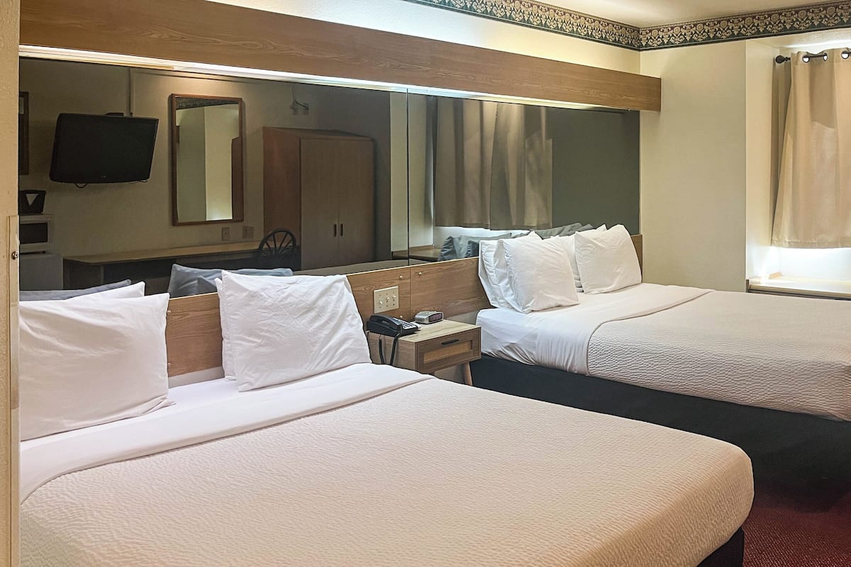 Hotellihuone, jossa on kaksi sänkyä, suuri peili, televisio ja ikkuna, jossa on verhot.