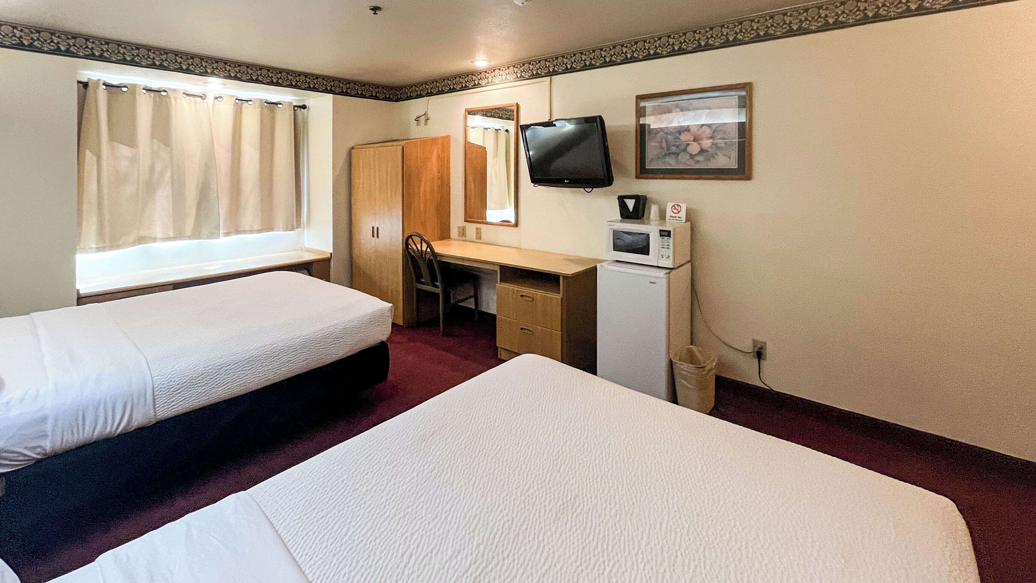 A hotel room with two beds, a desk, a television, a microwave, and a trash can.