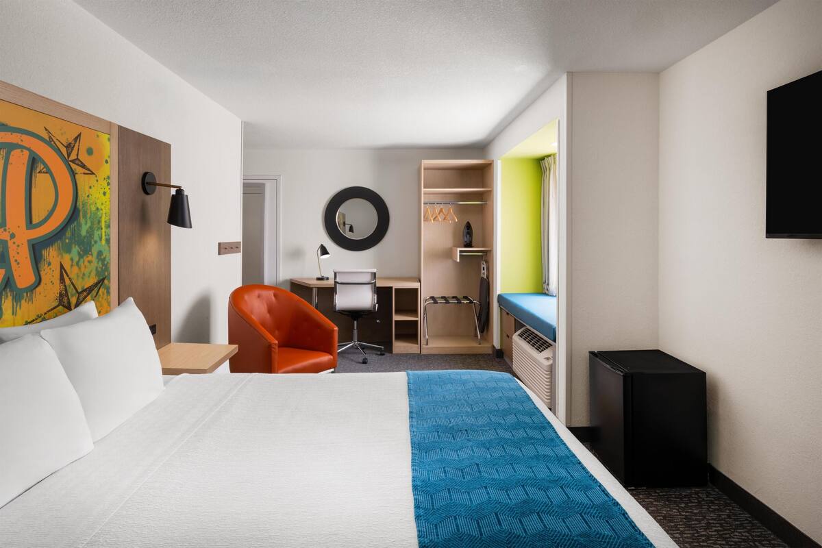 Una camera d'albergo con un letto, una poltrona arancione, una scrivania, uno specchio e una televisione.