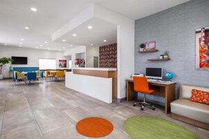 Un moderno vestíbulo de hotel con mostrador de recepción, zona de estar y estación de computadoras.