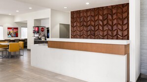A modern reception area with a white counter, a wooden patterned wall, and a seating area with yellow chairs.