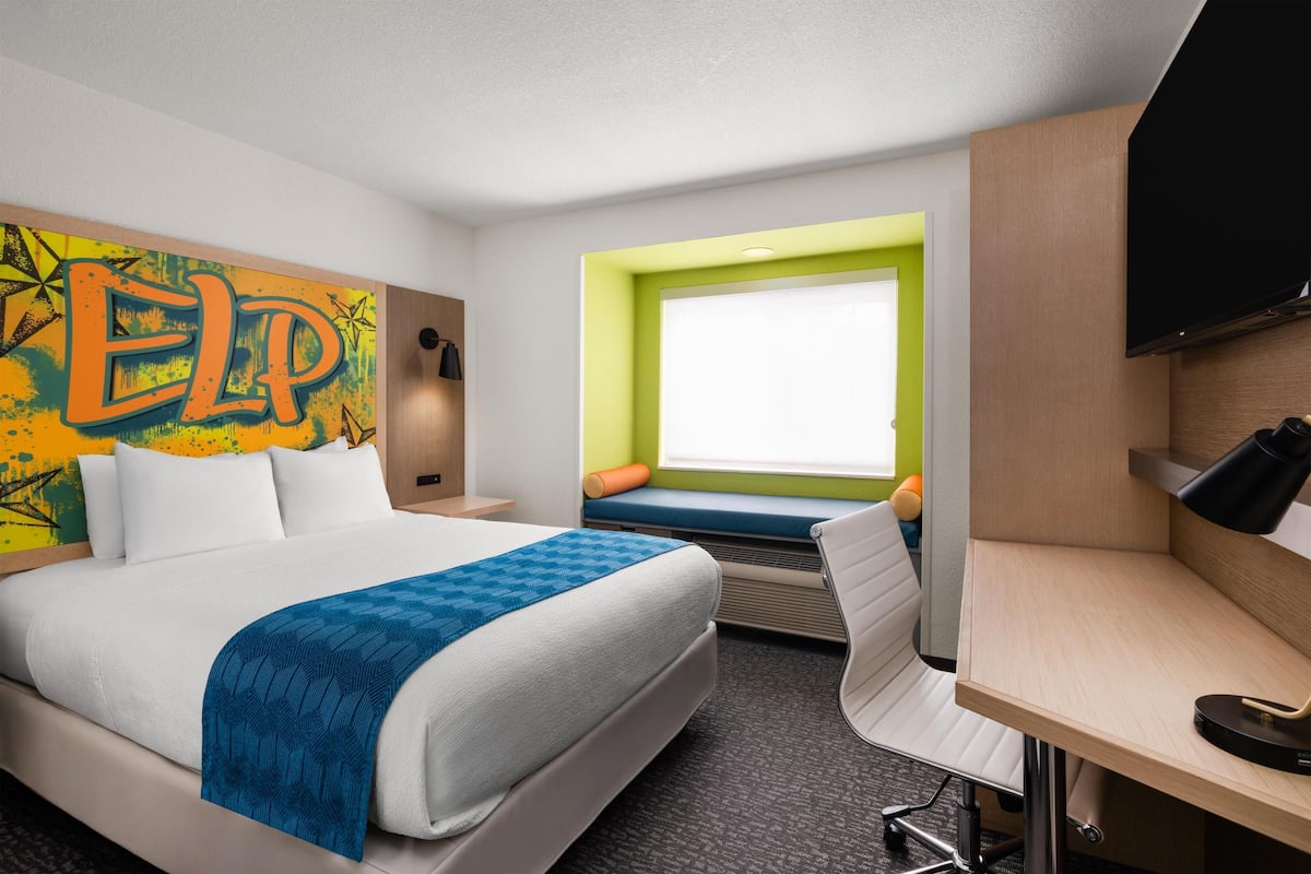 Camera d'albergo con un letto, una scrivania, una televisione, una finestra con vista e una decorazione murale colorata.