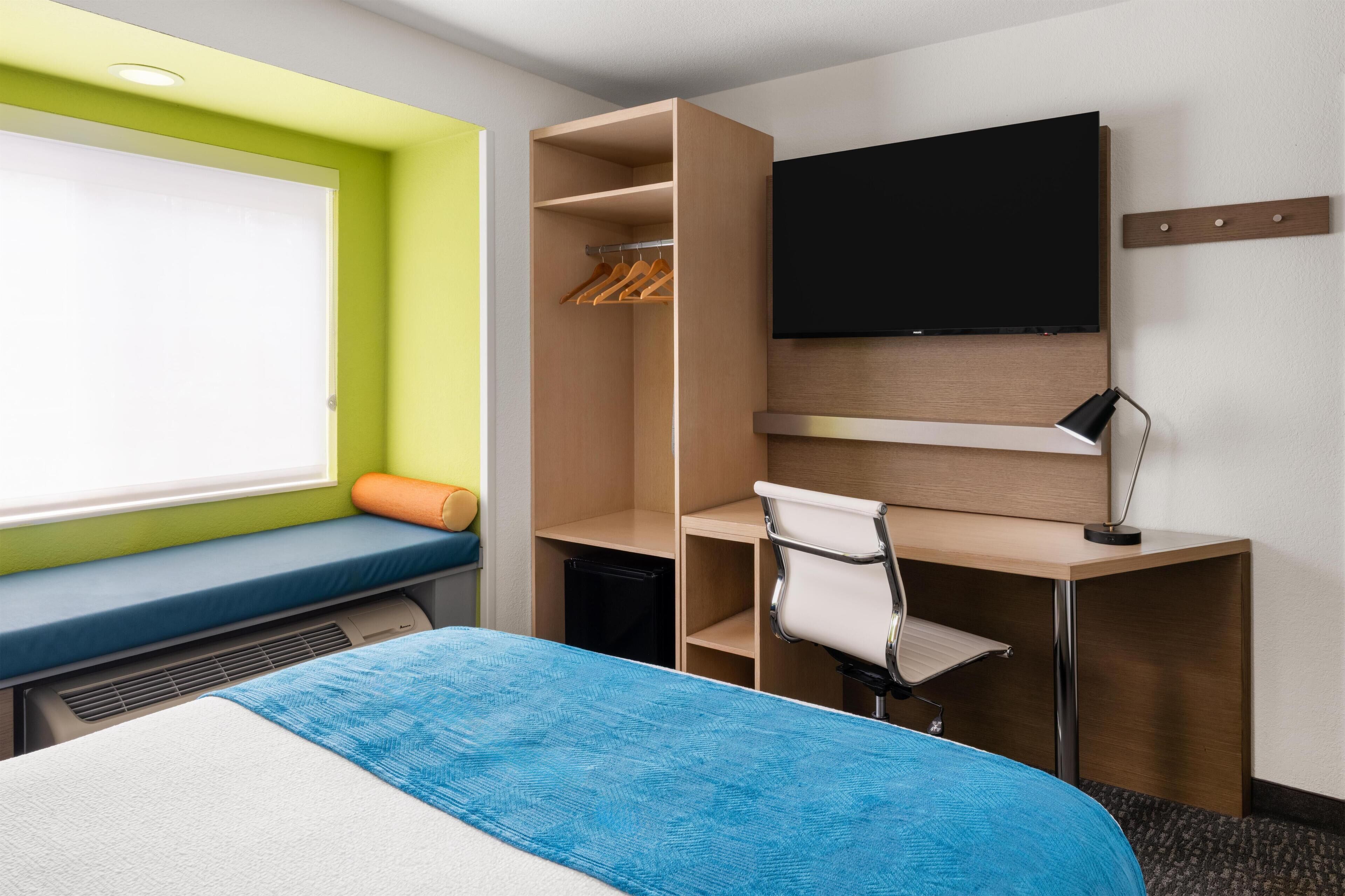 Een hotelkamer met een bed, een bureau met stoel, een televisie, een kledingkast en een raam.