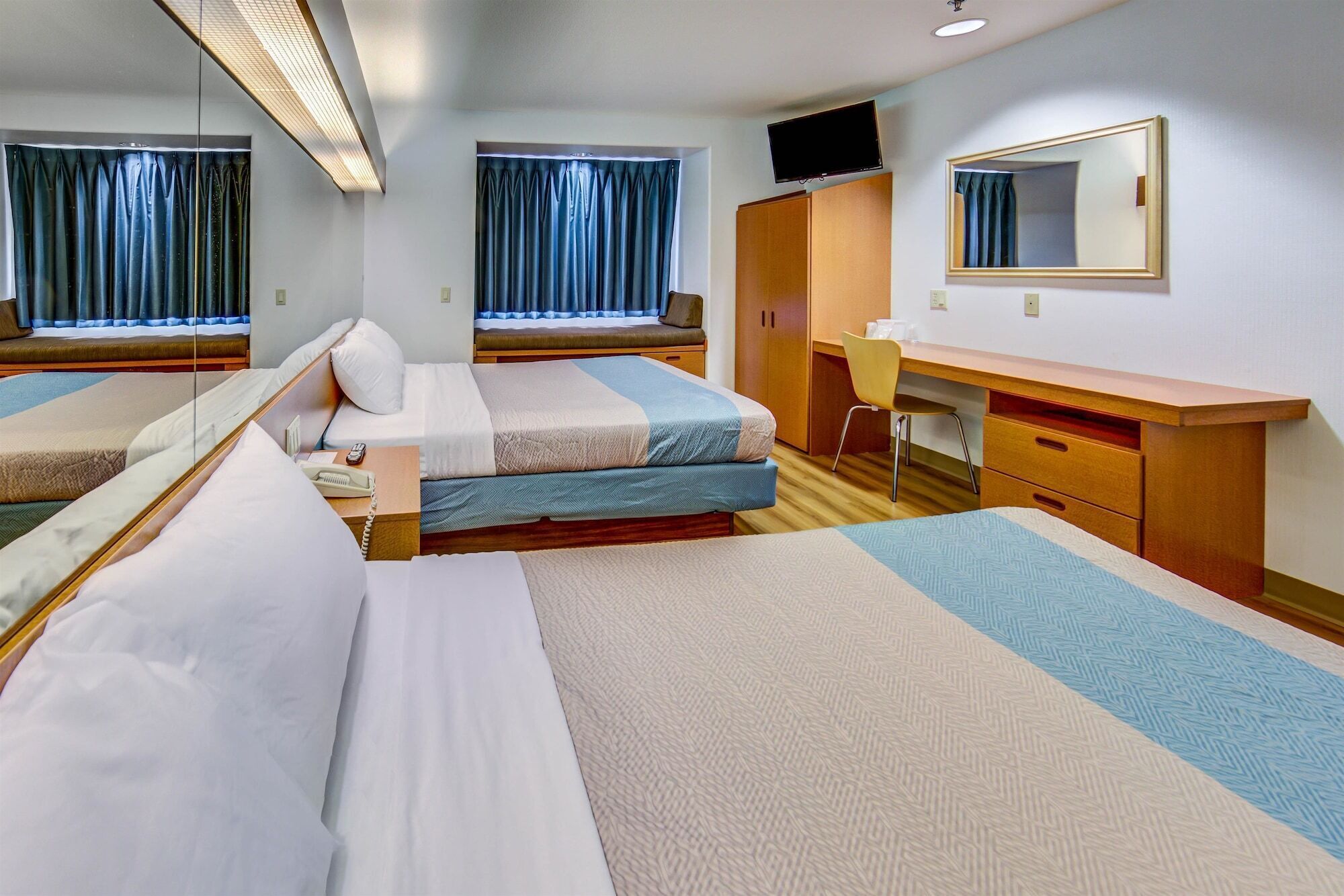 A hotel room with two beds, a desk, a chair, a TV, and a mirror.