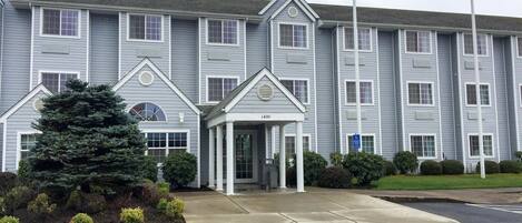 A multi-story building with a central entrance, flagpoles, and a well-maintained lawn.