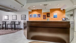 A reception area with a brown counter, framed pictures on the wall, and a seating area with chairs and a rug. - Motel 6 Sutherlin, OR (Sutherlin)