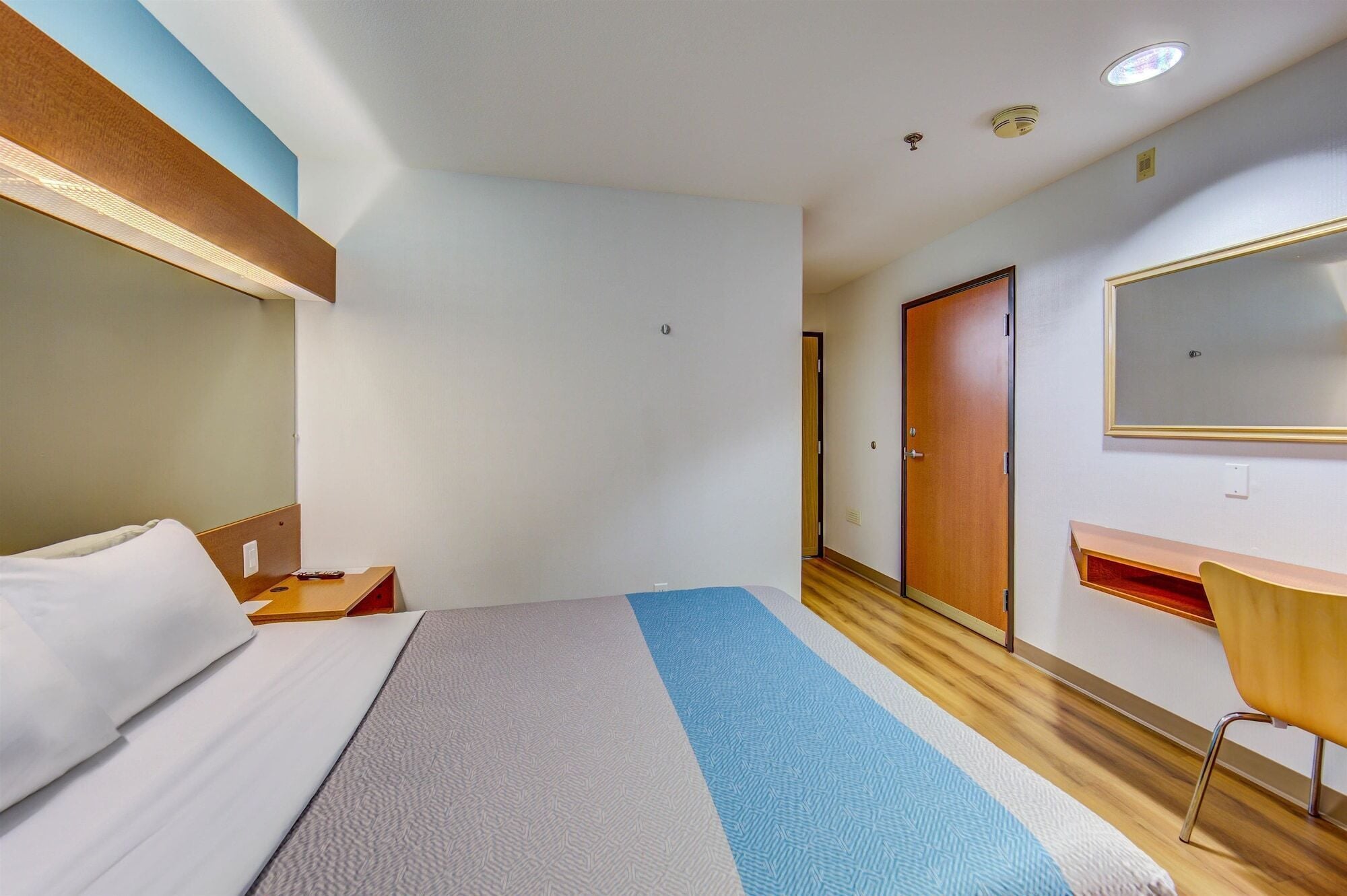 A hotel room with a bed, bedside table, chair, wardrobe, and a mirror on the wall.