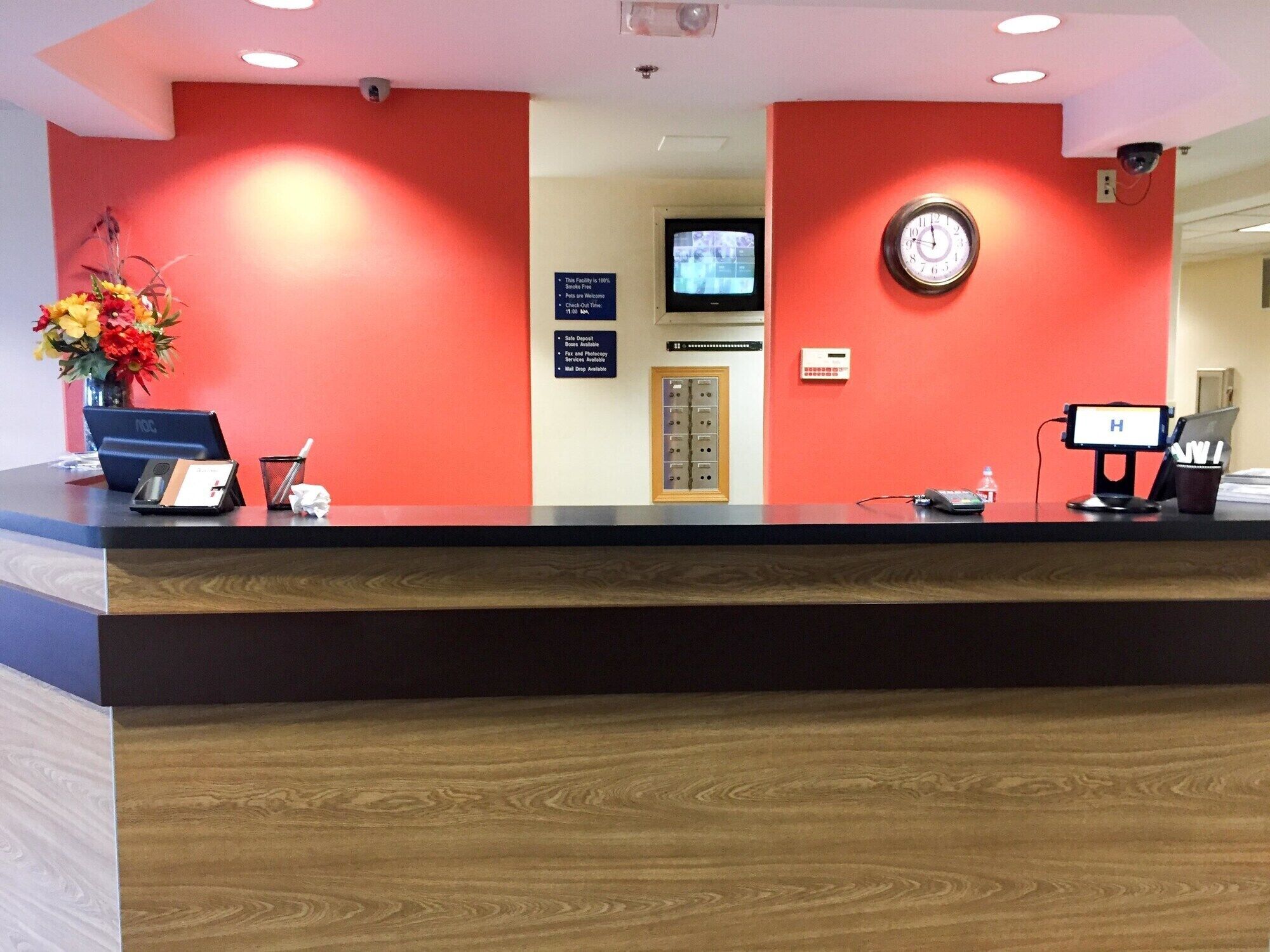 A hotel reception desk with a clock, a television, and a security camera.