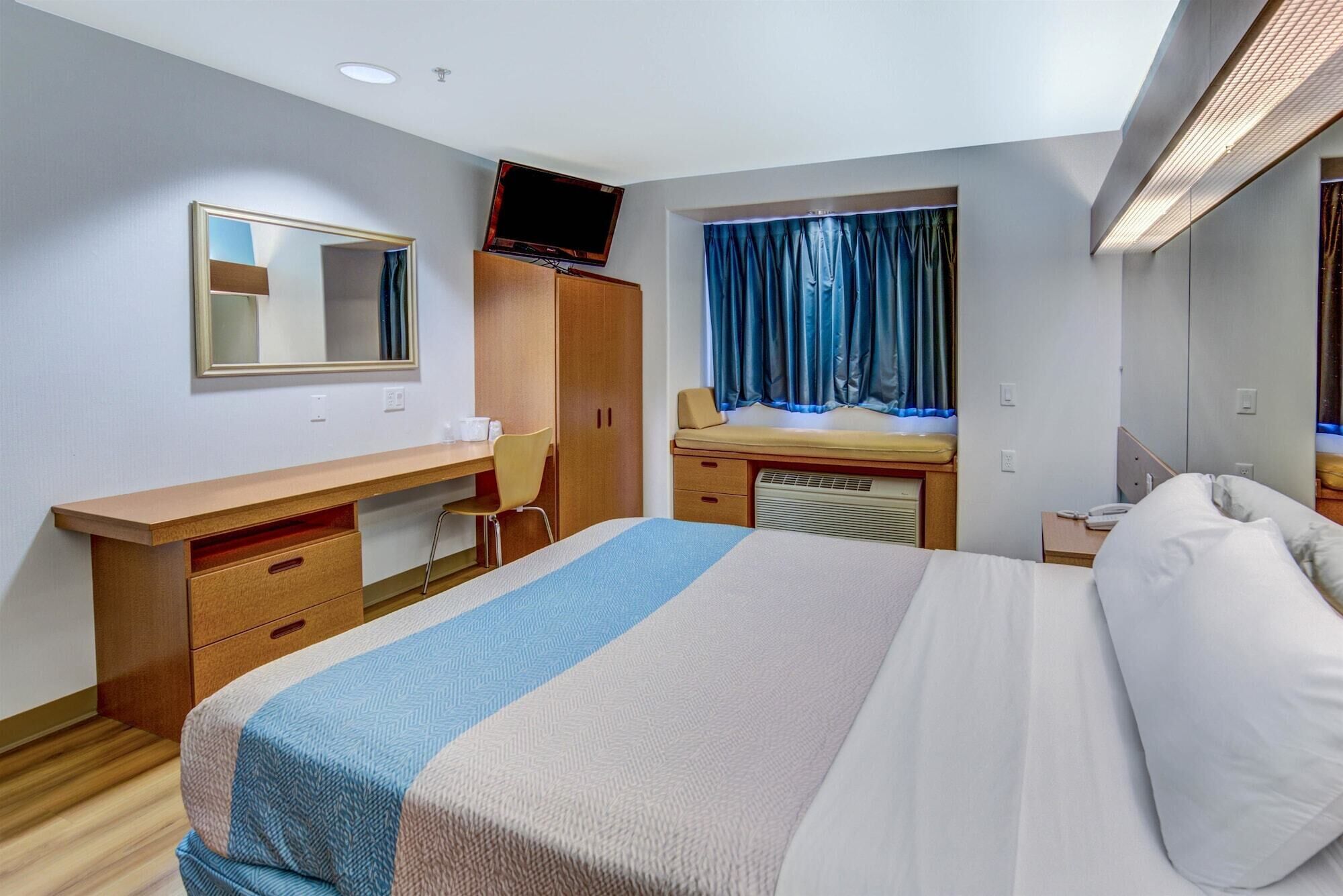 A hotel room with a bed, a desk, a chair, a television, and a window with curtains.