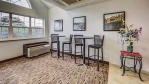 A room with a large window, a radiator, a table with chairs, and framed pictures on the wall. - Motel 6 Sutherlin, OR (Sutherlin)