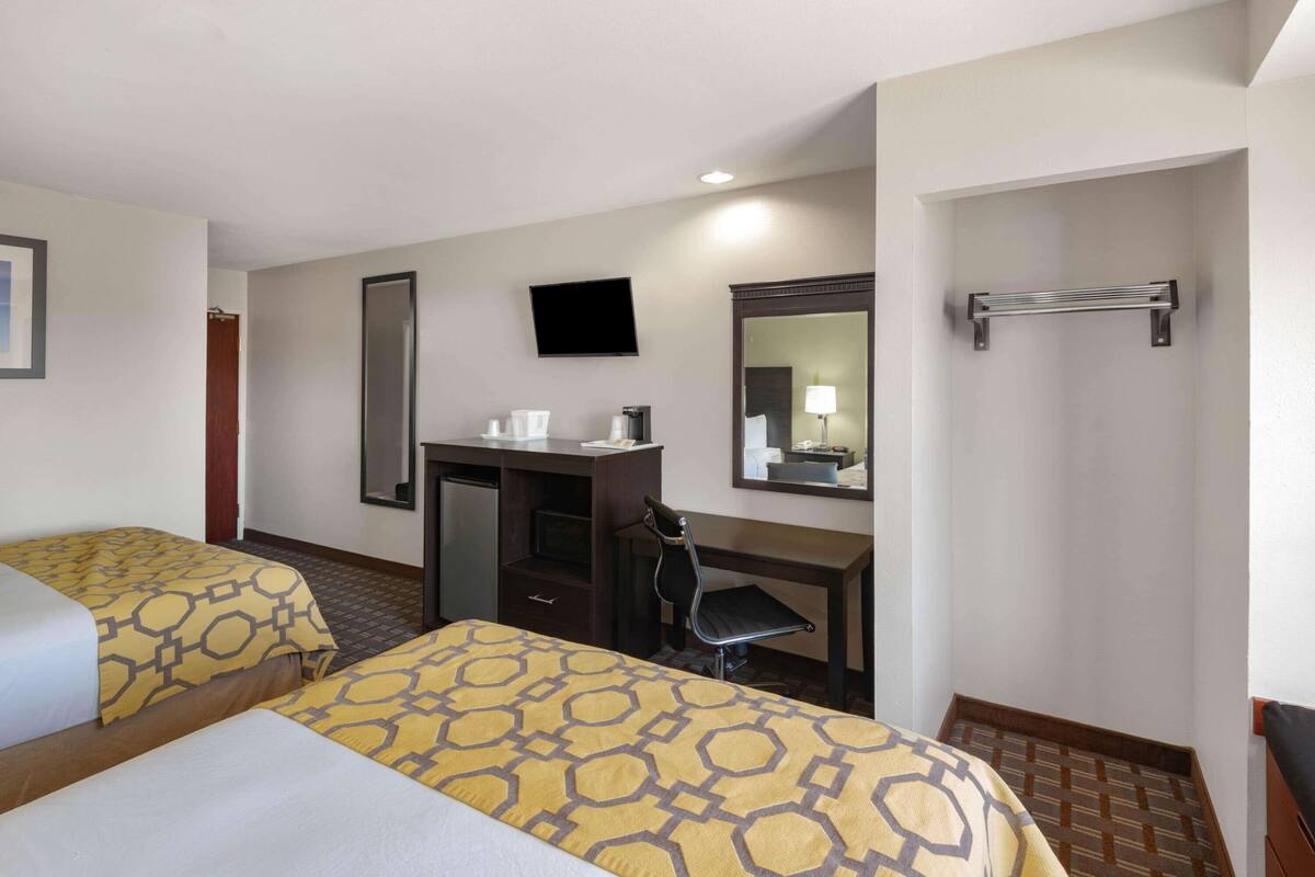 A hotel room with two beds, a desk, a chair, a TV, and a mirror.