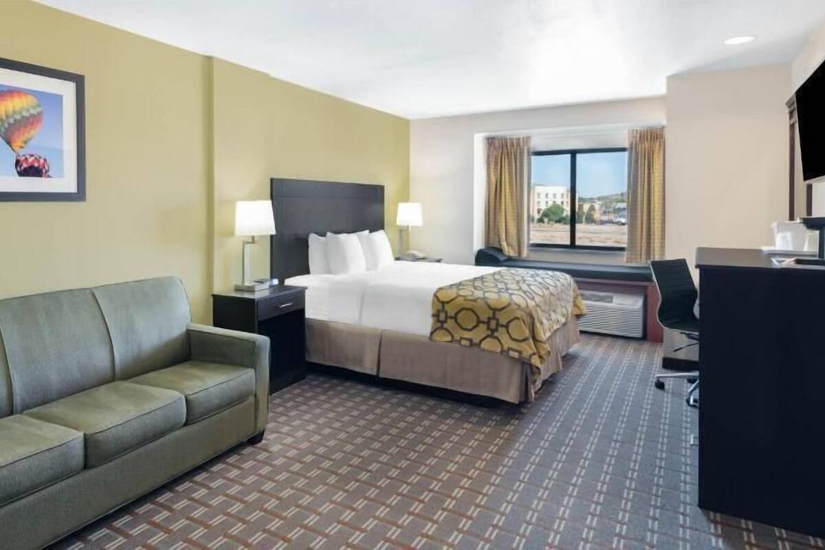 A hotel room with a bed, a sofa, a desk, and a window with curtains.