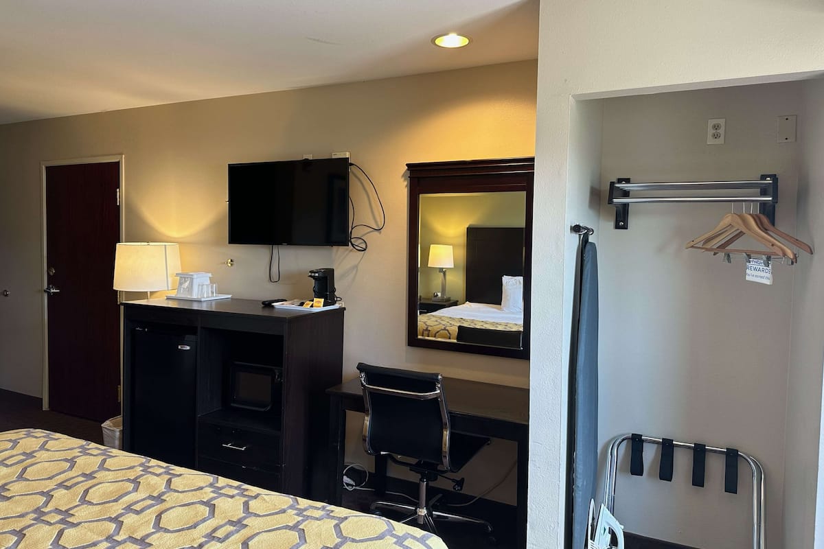 A hotel room with a bed, desk, chair, TV, mirror, and a coat rack.