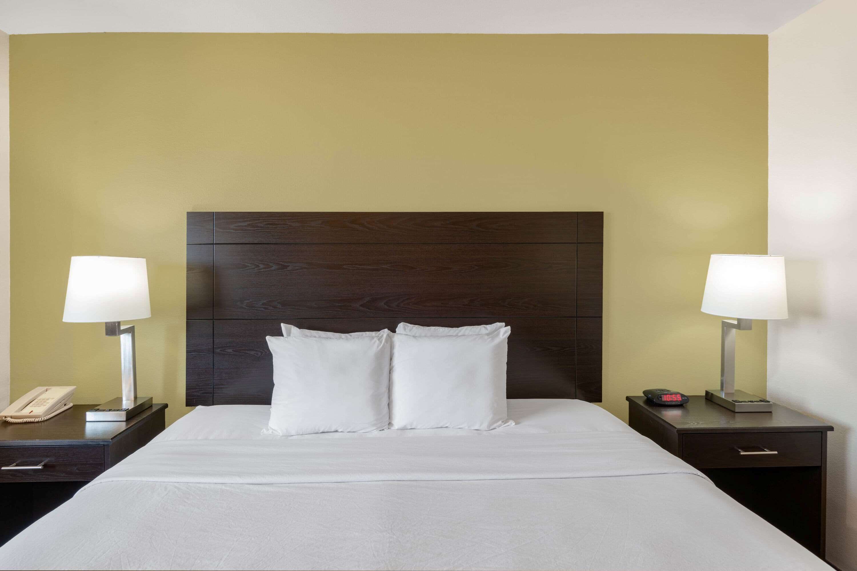 Une chambre d’hôtel avec un grand lit, deux tables de chevet, une petite table, une lampe, un téléphone et une horloge.