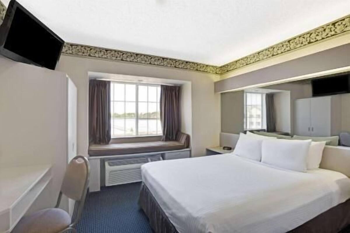 A hotel room with a bed, a desk, a chair, a television, a window with curtains, and a view of the outdoors.