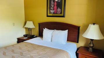 A hotel room with a bed, two bedside tables, a nightstand, a lamp, and a framed artwork on the wall.