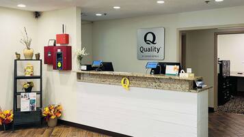 A hotel reception desk with a 'Quality by Choice Hotels' sign, a red information kiosk, and a plant display.