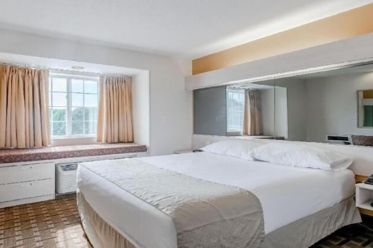 Habitación de hotel con una cama grande, una ventana con cortinas, una mesita de noche y un espejo.
