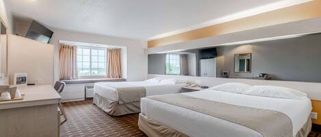 A hotel room with two beds, a desk, a window with curtains, a flat-screen TV mounted on the wall, and a mirror above the bed.