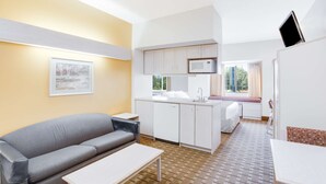 A compact living space with a kitchenette, a sofa, a dining table, and a window providing natural light.