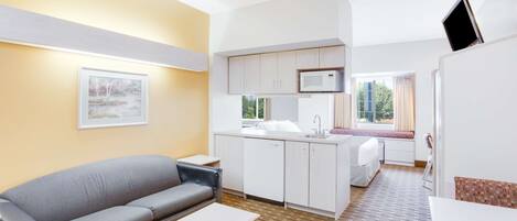 Un espacio habitable compacto con kitchenette, un sofá, una mesa de comedor y una ventana que proporciona luz natural.