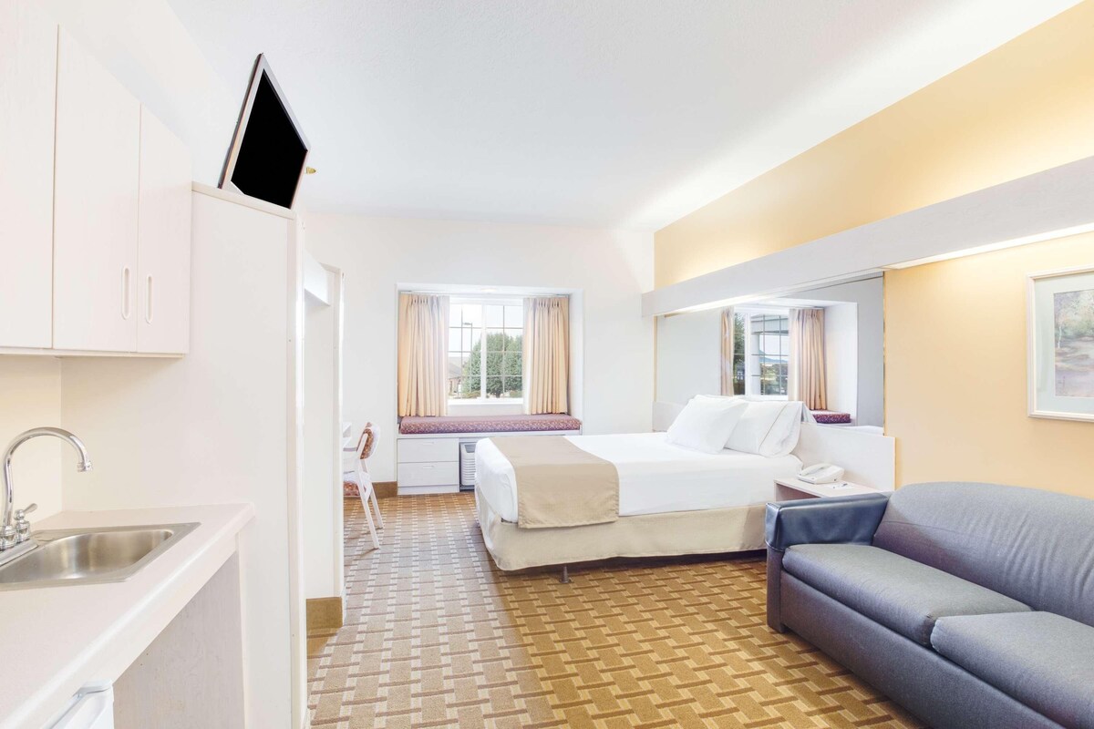 Habitación de hotel con cama, sofá, escritorio, ventana con cortinas, televisor de pantalla plana en la pared y suelo estampado.