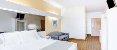 Una habitación de hotel con una cama grande, un escritorio con una computadora, una silla, una kitchenette pequeña y un televisor montado en la pared.