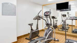 A fitness room with exercise bikes, a treadmill, and a TV screen.