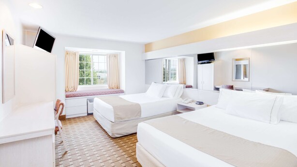 A hotel room with two beds, a desk, a TV, and a window with curtains.