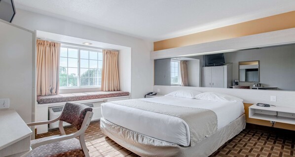 Habitación de hotel con cama, escritorio, silla, ventana con cortinas, televisor y espejo.