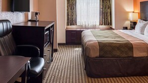 A hotel room with a bed, a desk with a chair, a TV mounted on the wall, and a window with curtains.