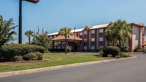 A hotel with a prominent EconoLodge Inn & Suites sign, featuring a multi-story building with a red and beige color scheme, surrounded by well-maintained landscaping and palm trees.