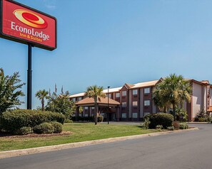 A hotel with a prominent EconoLodge Inn & Suites sign, featuring a multi-story building with a red and beige color scheme, surrounded by well-maintained landscaping and palm trees. - Econo Lodge Inn & Suites Natchitoches (Natchitoches)