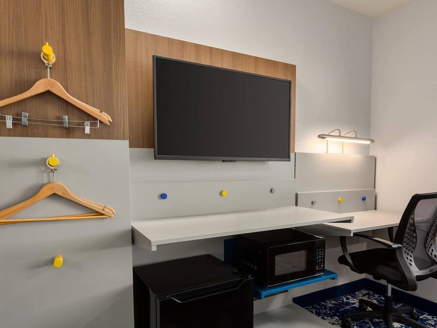 Una habitación moderna con televisor montado, escritorio, silla y microondas.