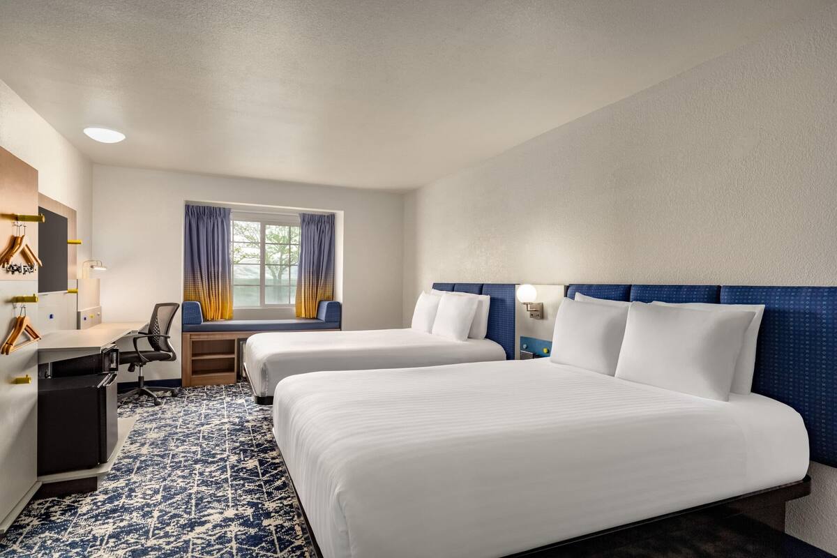 Habitación de hotel con dos camas, un escritorio, una silla, una mesita y una ventana con cortinas.
