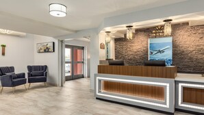 A reception area with a stone wall, a reception desk, two armchairs, and a poster of an airplane. - Microtel Inn & Suites by Wyndham Salt Lake City Airport (Salt Lake City)