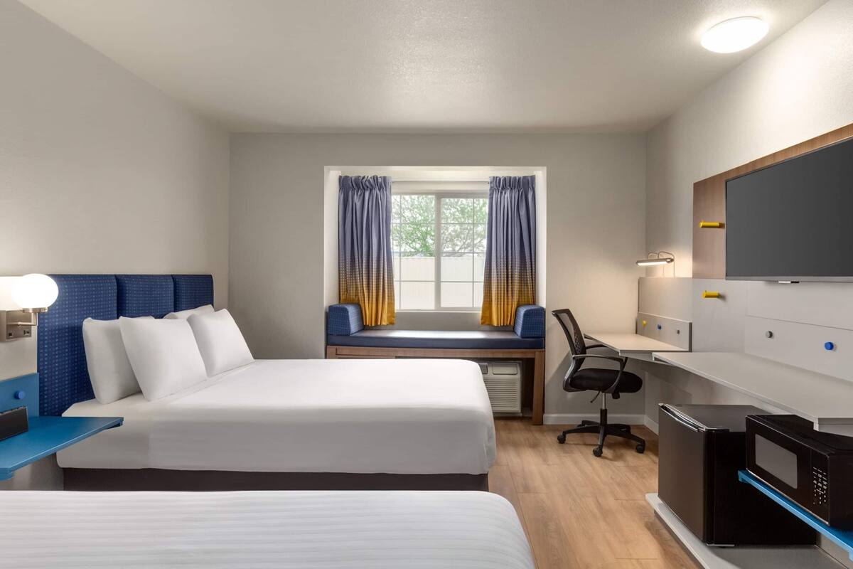 Una habitación de hotel con cama, escritorio, silla, televisor y microondas.