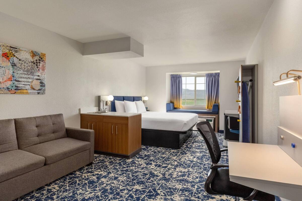 Una habitación de hotel con sofá, cama, escritorio y ventana con cortinas.
