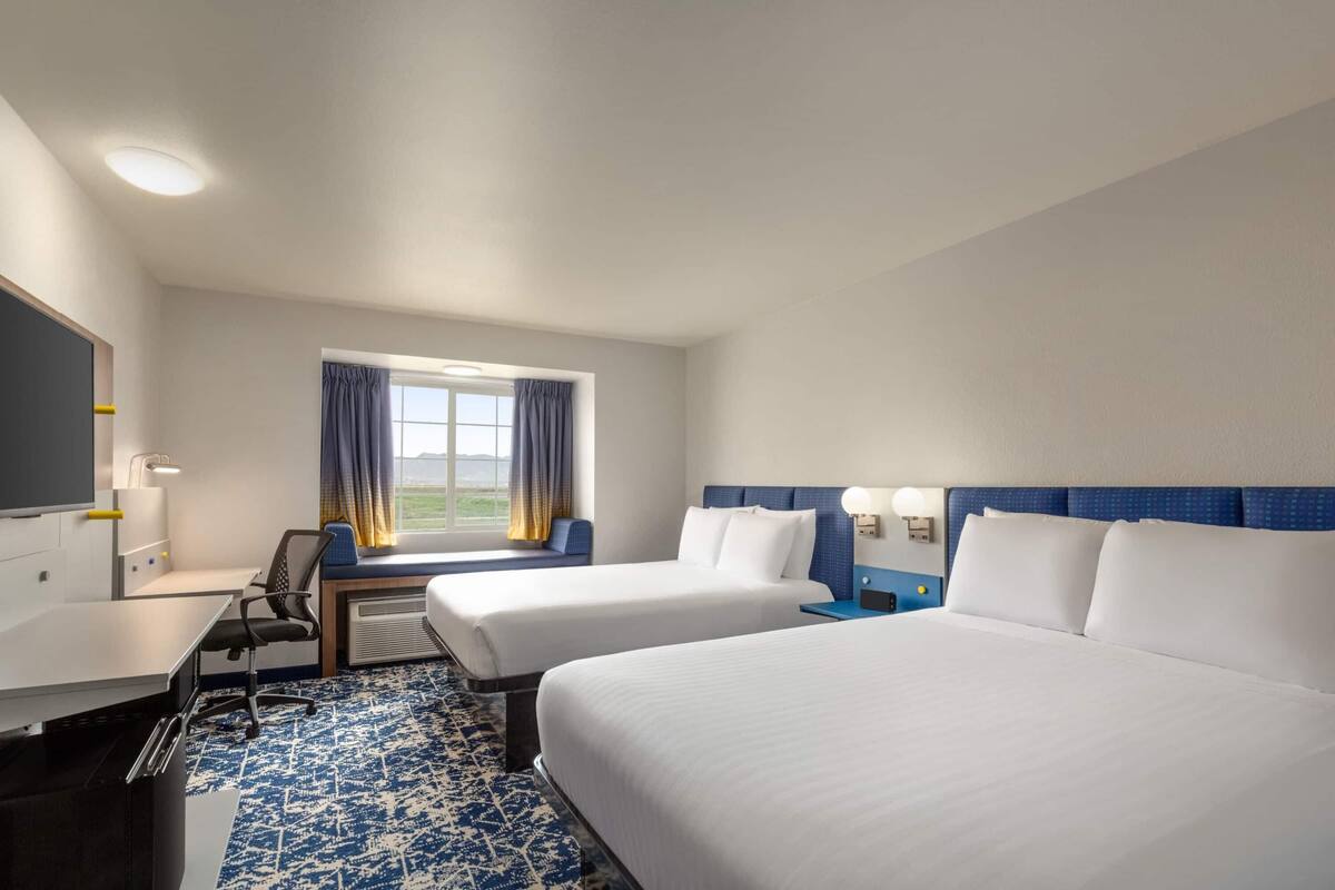 Habitación de hotel con dos camas, un escritorio, una silla, un ventanal con cortinas y vistas al exterior.