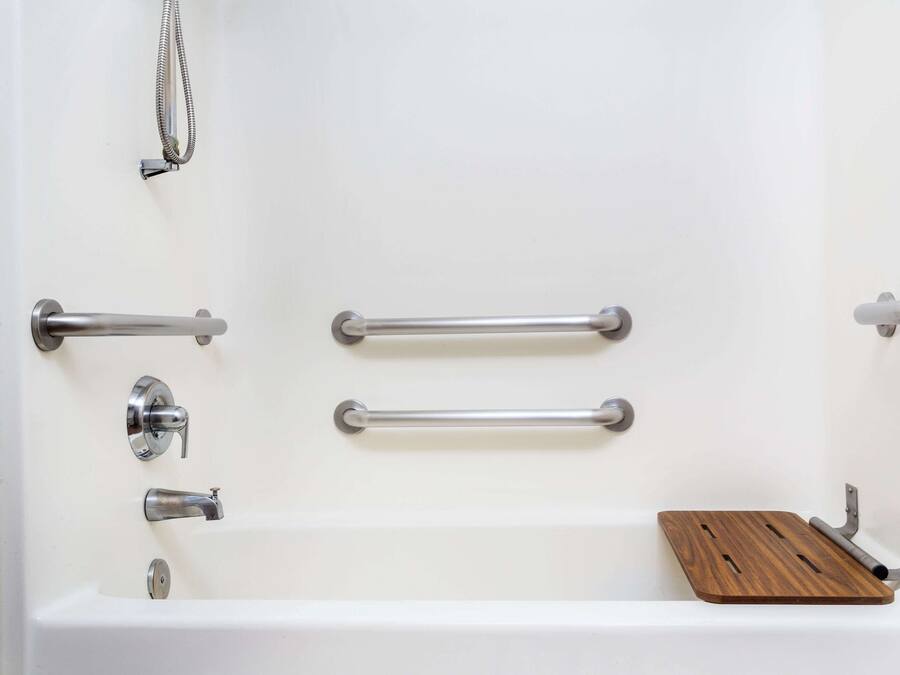 A white bathtub with two metal grab bars, a wooden shelf, and a showerhead.