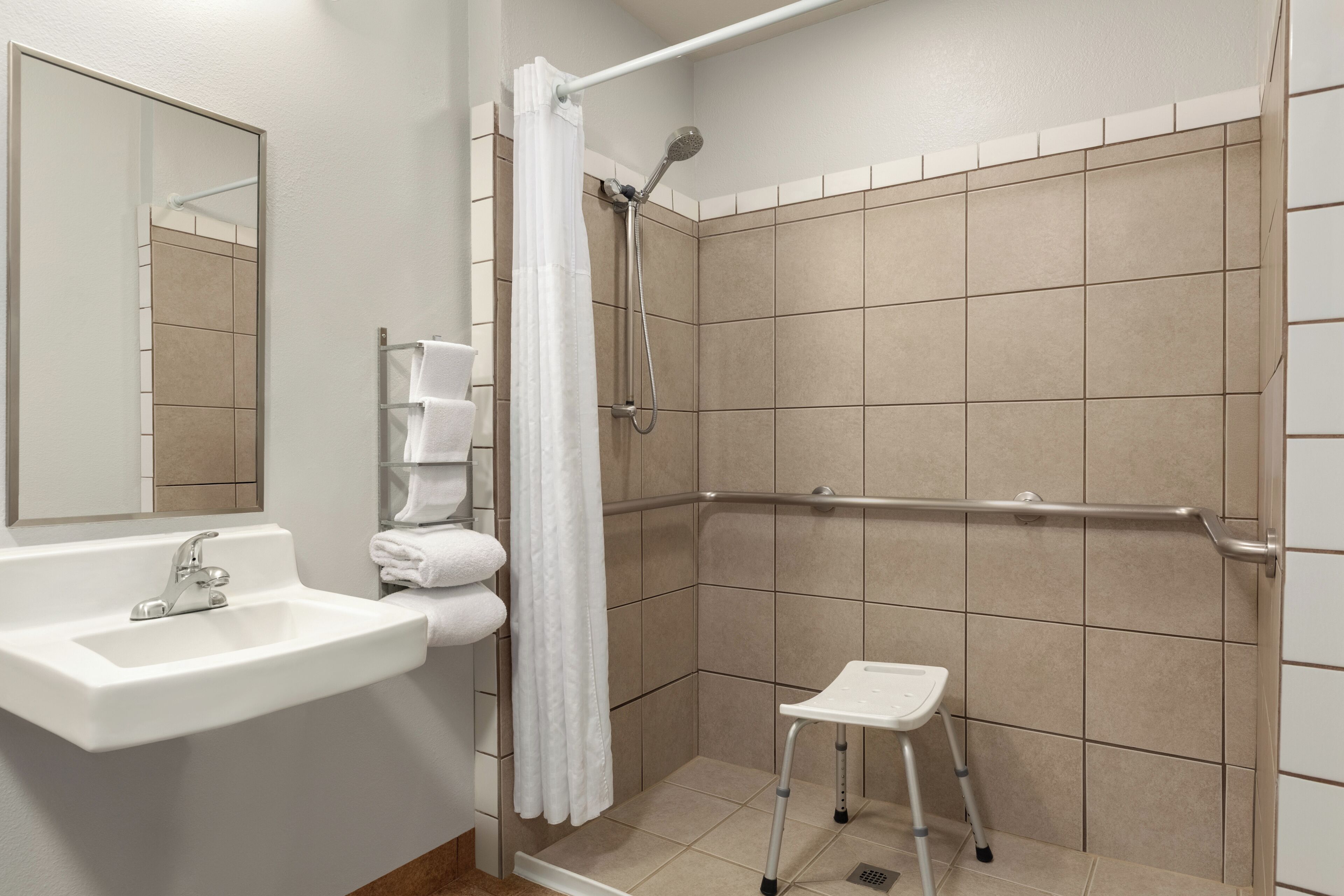 Un baño con lavamanos, espejo, ducha y un pequeño taburete.