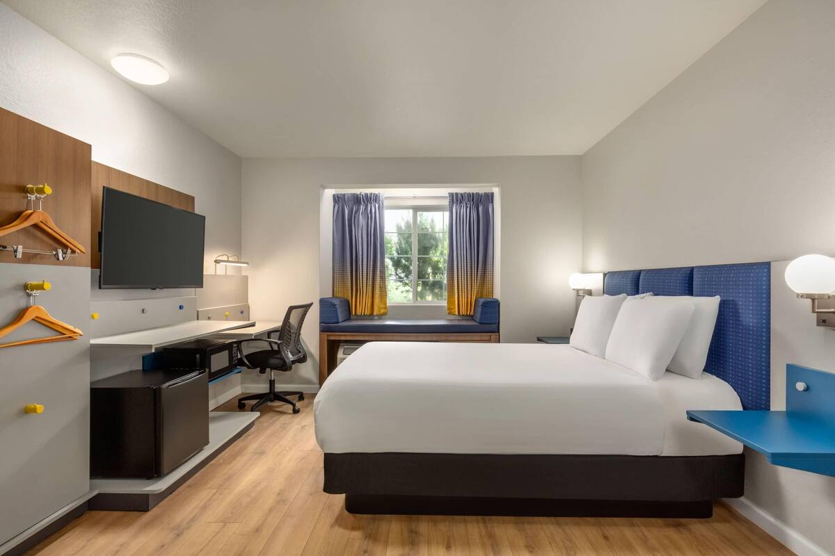 Habitación de hotel con cama, escritorio, silla, televisor y ventana con cortinas.