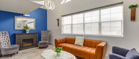 A living room with a fireplace, a large window, and a blue accent wall.