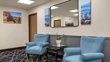 A hotel lobby with two blue armchairs, a small table with a plant, and two framed cityscape pictures on the wall.