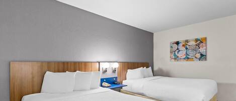 A hotel room with two beds, a wooden headboard, a nightstand with a phone, and a wall art piece.